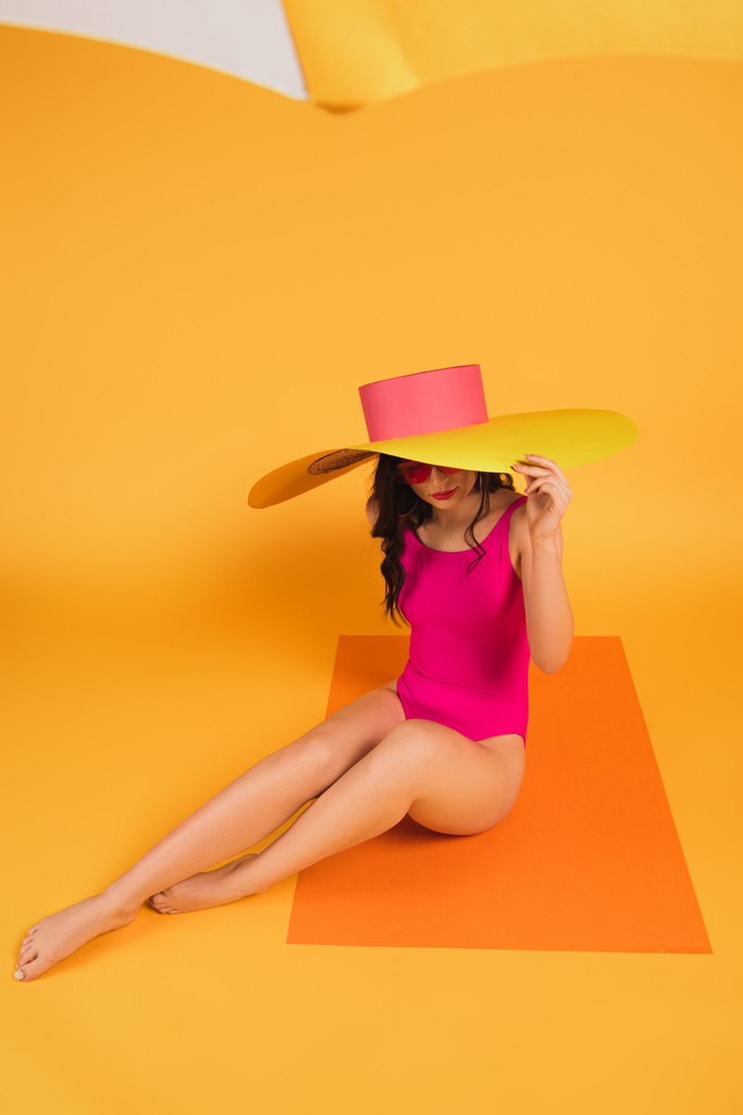 селективное внимание стильной женщины в соломенной шляпе и купальнике, сидящей на желтом
 - Фото, изображение