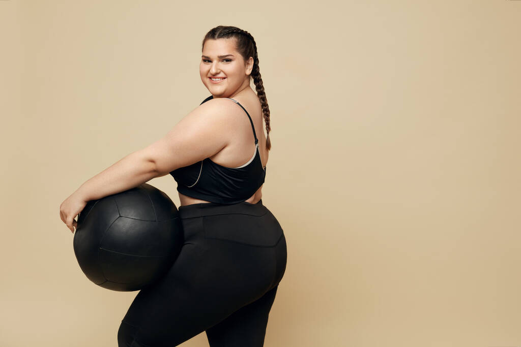 Plus Size Model. Plnohodnotná žena v černém sportovním oblečení Portrét. Bruneta drží Fitness Ball. Body pozitivní a sport jako životní styl. - Fotografie, Obrázek