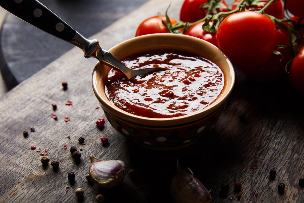 delicioso molho de tomate na tigela com colher perto de tomates e especiarias na tábua de madeira
 - Foto, Imagem
