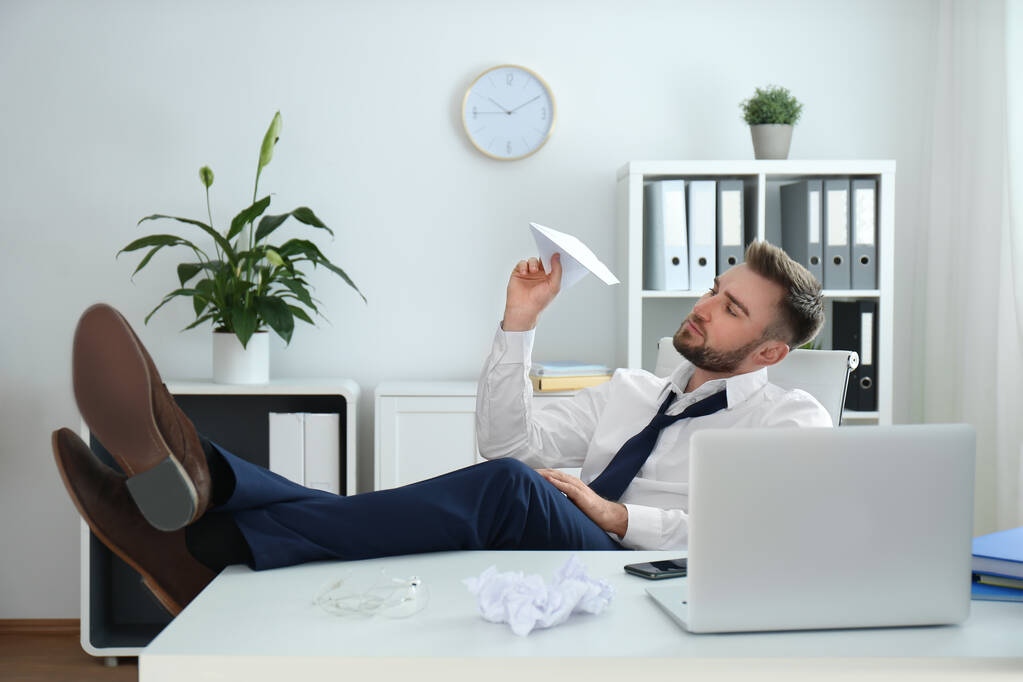 Ленивый молодой человек играет с бумажным самолетом в офисе
 - Фото, изображение