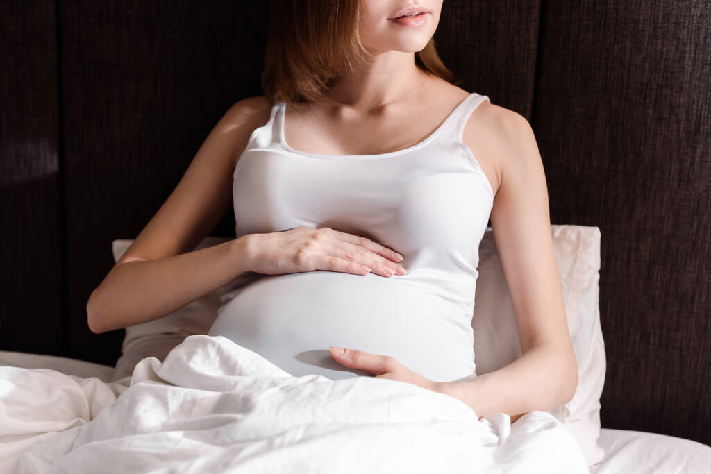 oříznutý pohled těhotné ženy dotýkající se břicha v posteli  - Fotografie, Obrázek