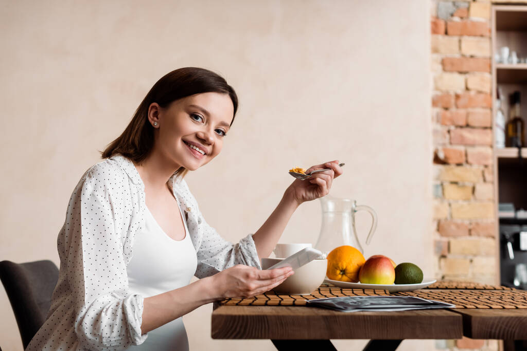 onnellinen raskaana oleva nainen tilalla lusikka maissi hiutaleet ja älypuhelin
  - Valokuva, kuva