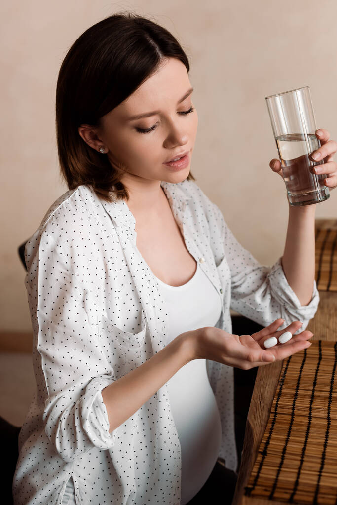 ελκυστική έγκυος γυναίκα που κατέχουν βιταμίνες χάπια και ένα ποτήρι νερό  - Φωτογραφία, εικόνα