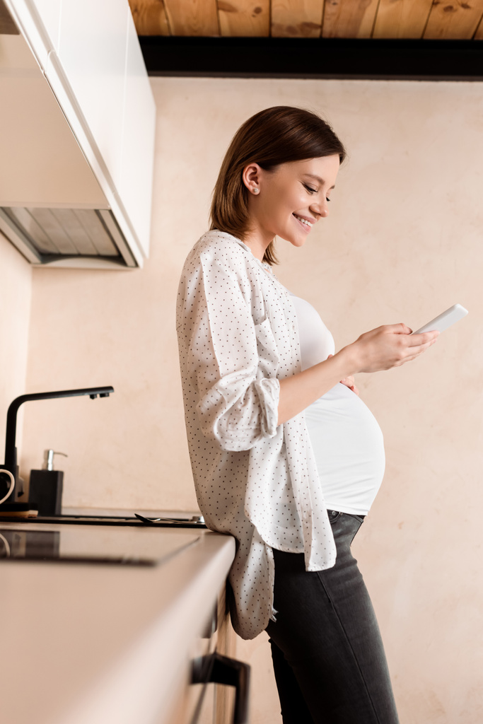 вид збоку щасливої вагітної жінки за допомогою смартфона
  - Фото, зображення