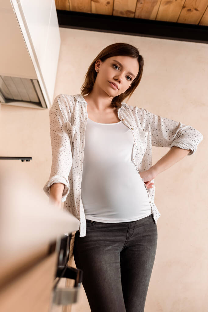 enfoque selectivo de la mujer embarazada de pie con la mano en la cadera
 - Foto, Imagen