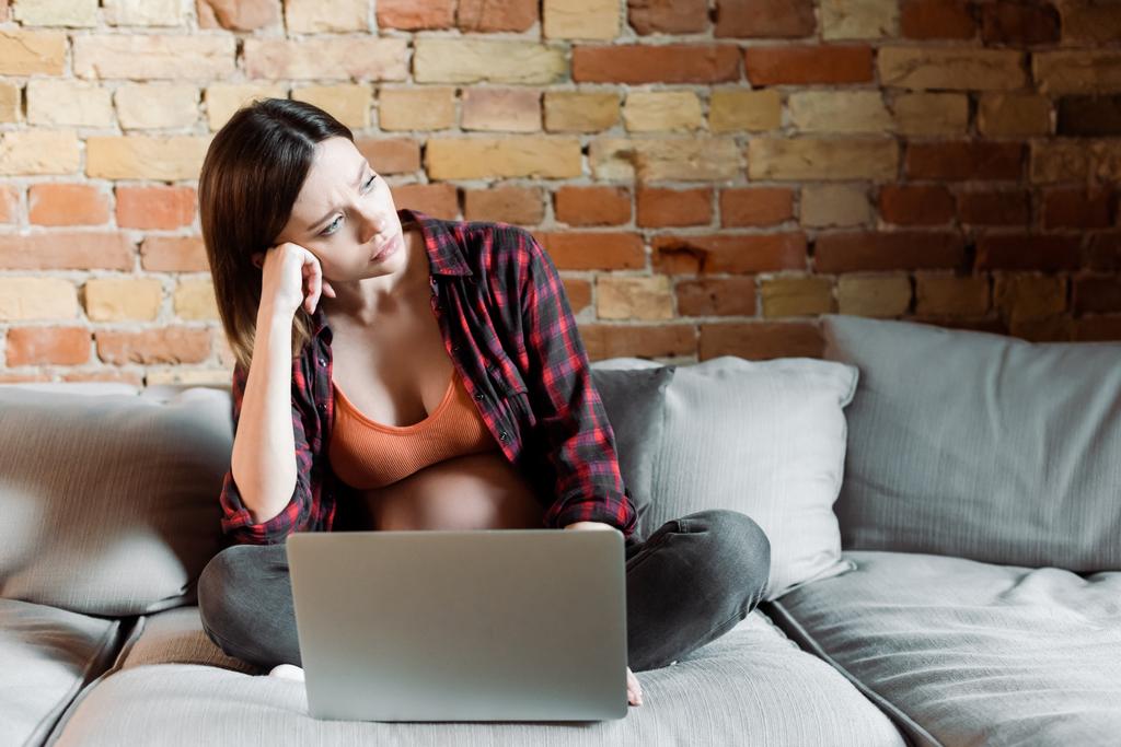 sconvolto e incinta freelance guardando lontano vicino laptop in soggiorno
  - Foto, immagini
