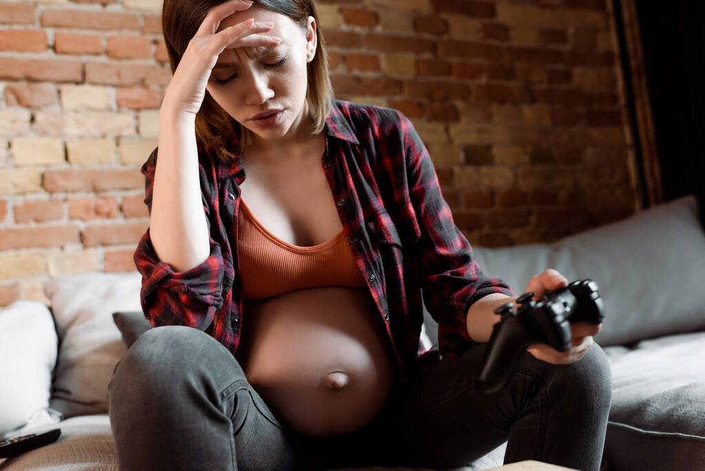 KYIV, UCRANIA - 30 de abril de 2020: enfoque selectivo de la mujer molesta y embarazada sosteniendo el joystick en la sala de estar
  - Foto, imagen