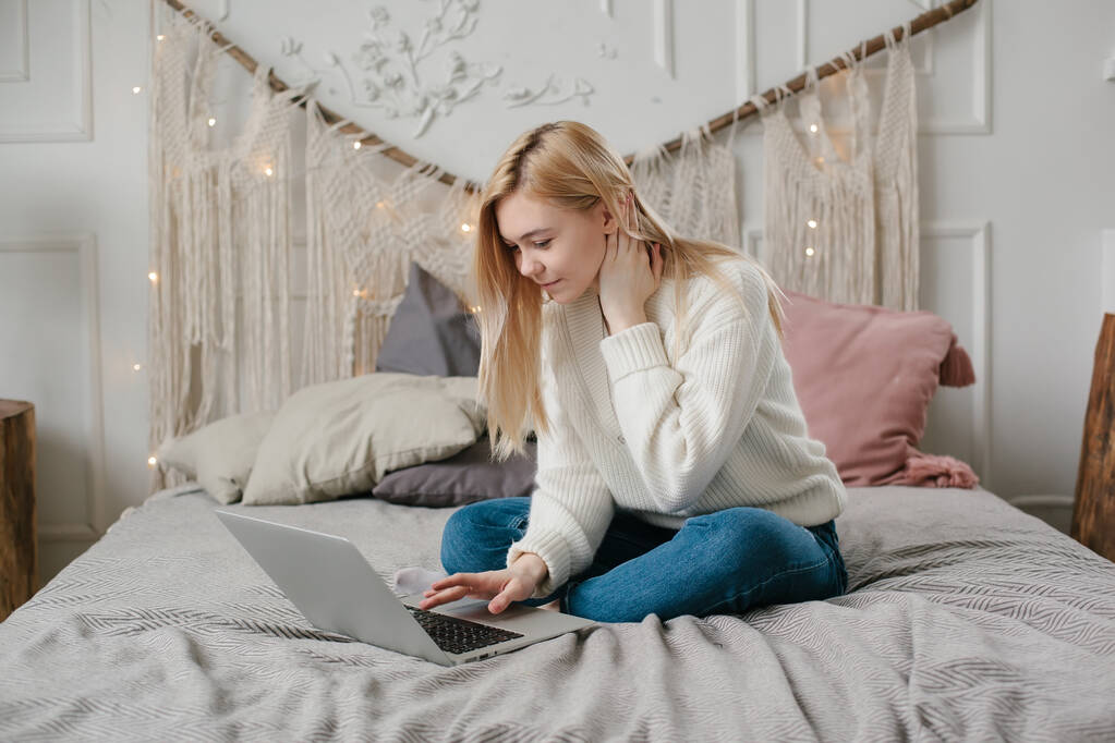 Chica estudiante de estudio en línea con el profesor de Skype, mujer joven y feliz mira el ordenador portátil sentarse en la cama en casa
. - Foto, imagen
