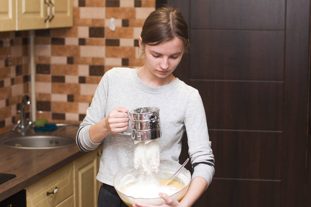 La fille versera de la farine dans la pâte. La fille cuisine. Mains préparant la pâte. Femme pétrissant pâte fraîche pour la fabrication
 - Photo, image