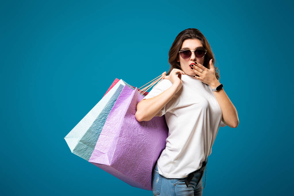 Güneş gözlüklü genç ve şık bir kız çok renkli alışveriş çantalarıyla yürüyor. Konsept alışveriş ve mağaza. - Fotoğraf, Görsel