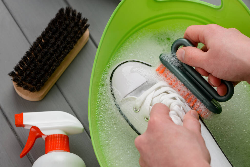 Muž si myje bílé tenisky štětcem a čisticím prostředkem - Fotografie, Obrázek
