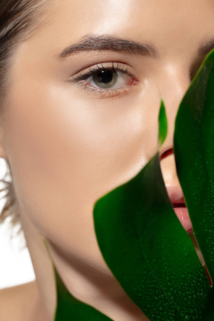 Bio. Großaufnahme einer schönen jungen Frau mit grünen Blättern vor weißem Hintergrund. Kosmetik und Make-up, natürliche und ökologische Behandlung, Hautpflege. - Foto, Bild