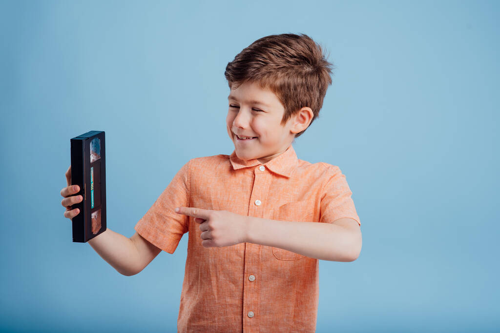 boldog kisfiú videokazettával, elszigetelt kék háttér, - Fotó, kép