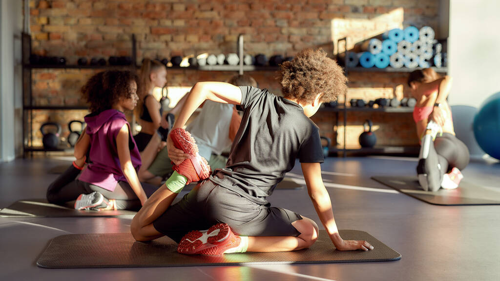 Mantenha seu corpo saudável. Tiro completo de menino tentando pose de ioga, fazendo exercícios com outras crianças e treinador feminino no ginásio. Alongamento em um dia ensolarado. Esporte, vida saudável, conceito de educação física
 - Foto, Imagem
