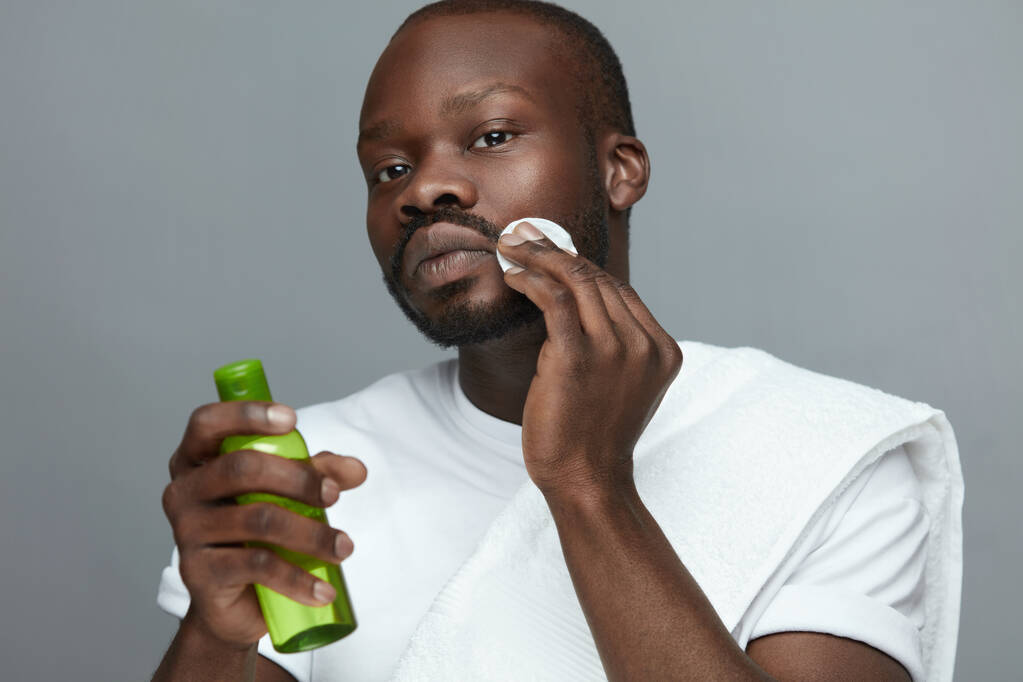 Arcápolás. Férfi afrikai modell tisztítja arc bőr kerek folt. Zöld palack kozmetikai tonikkal. Bőrápolás szépség rutin az ember számára. - Fotó, kép