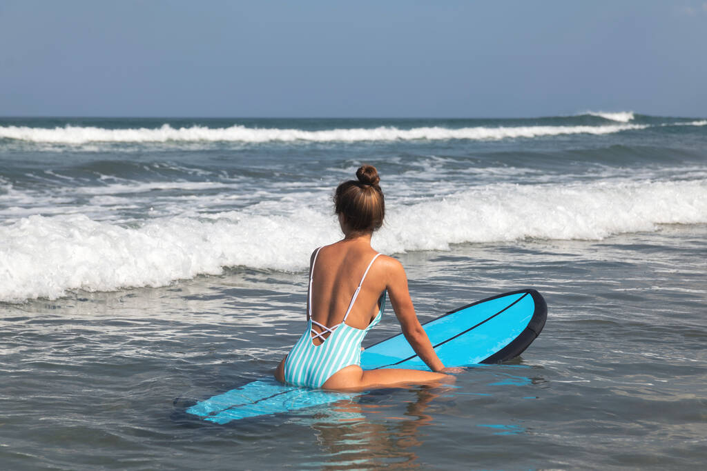 Mujer joven surfista está sentado en la tabla larga y tratando de coger la ola
  - Foto, imagen