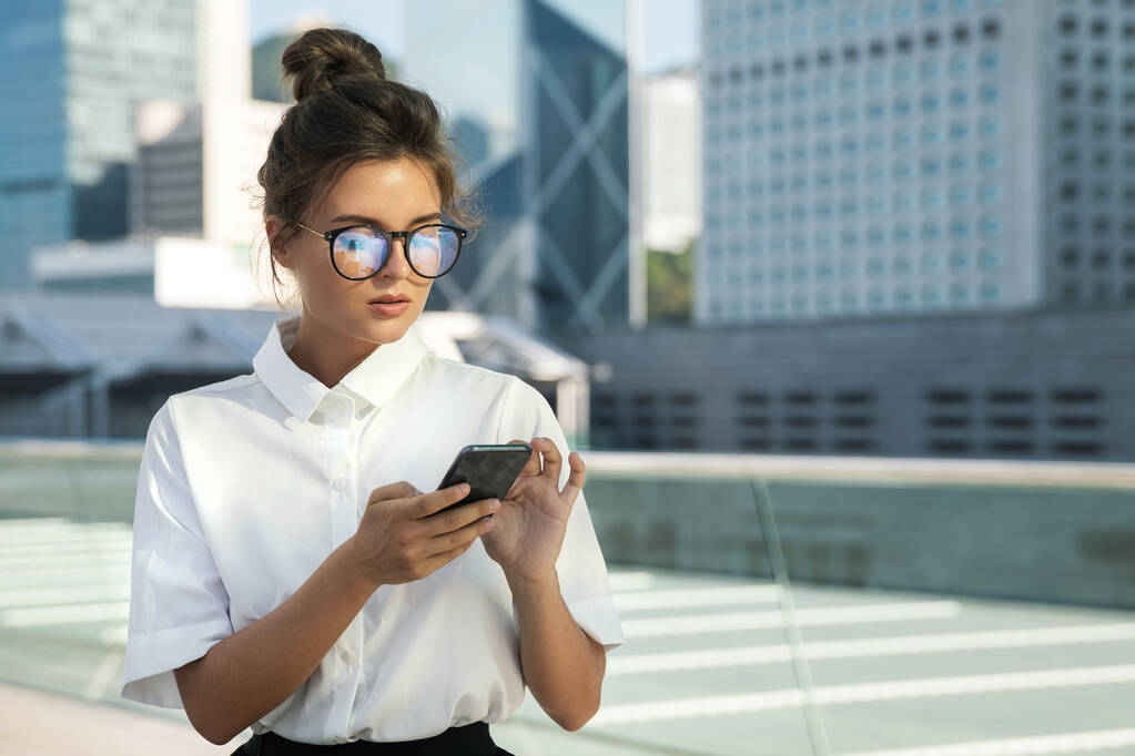 Young businesswoman is using smartphone in the city with modern buildings - Photo, Image