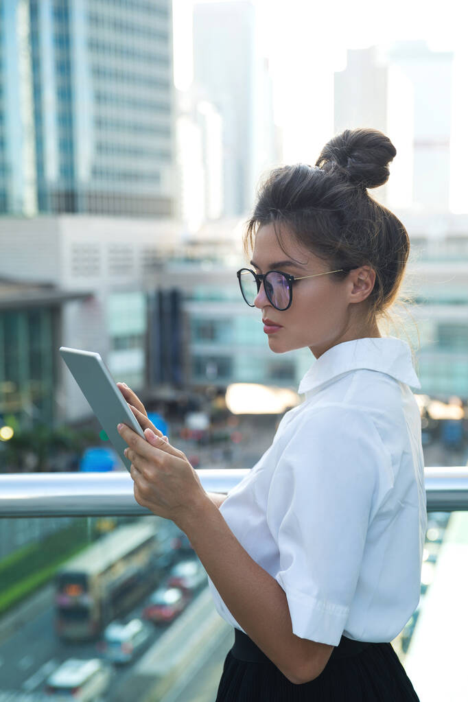 Молода жінка в розумному повсякденному одязі використовує планшетний ПК на вулицях сучасного міста
 - Фото, зображення