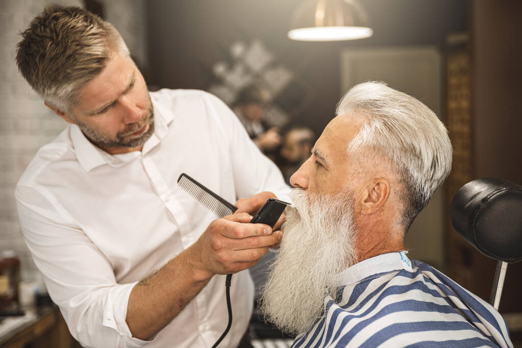 Handsome senior man getting styling and trimming of his beard in the barbershop - Photo, Image