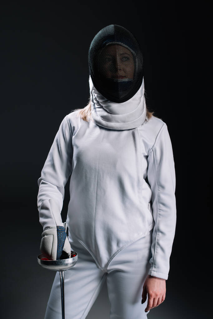 Fencer in fencing mask and suit holding rapier isolated on black  - Photo, Image
