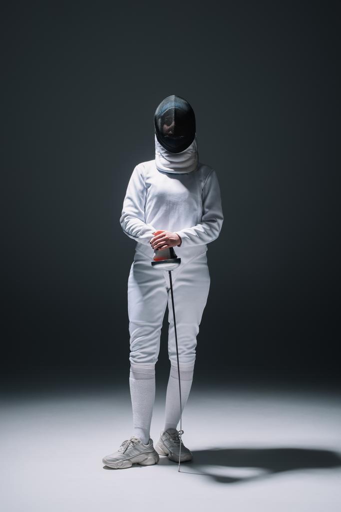 Fencer σε μάσκα ξιφασκίας και κοστούμι κρατώντας rapier κάτω από τα φώτα της δημοσιότητας σε μαύρο φόντο - Φωτογραφία, εικόνα