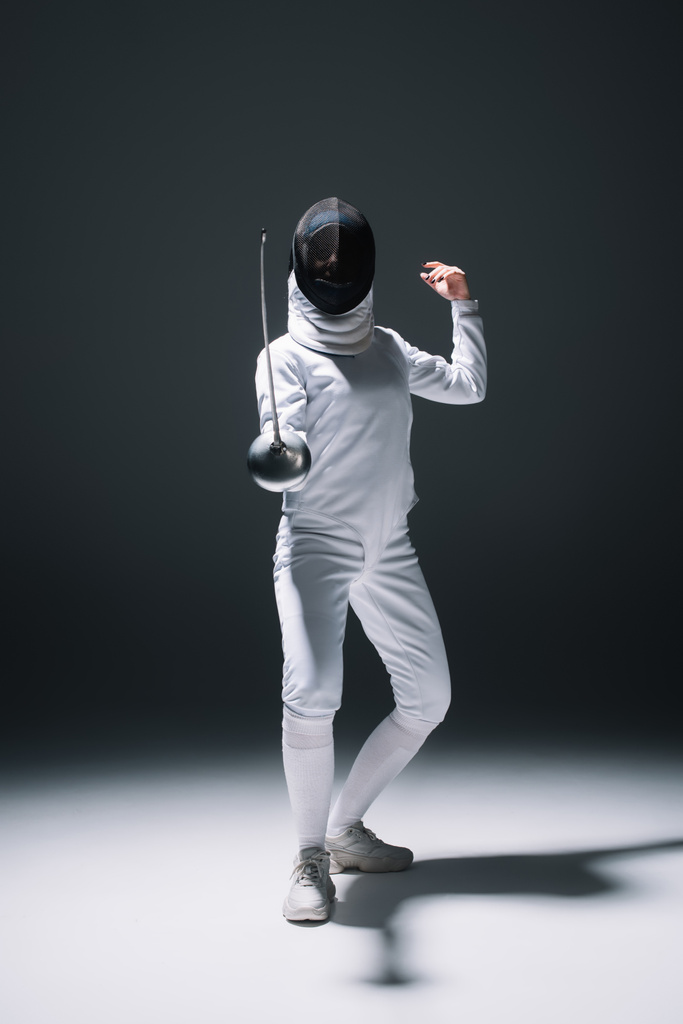 Fencer in hekwerk masker en pak training onder spotlight op zwarte achtergrond - Foto, afbeelding