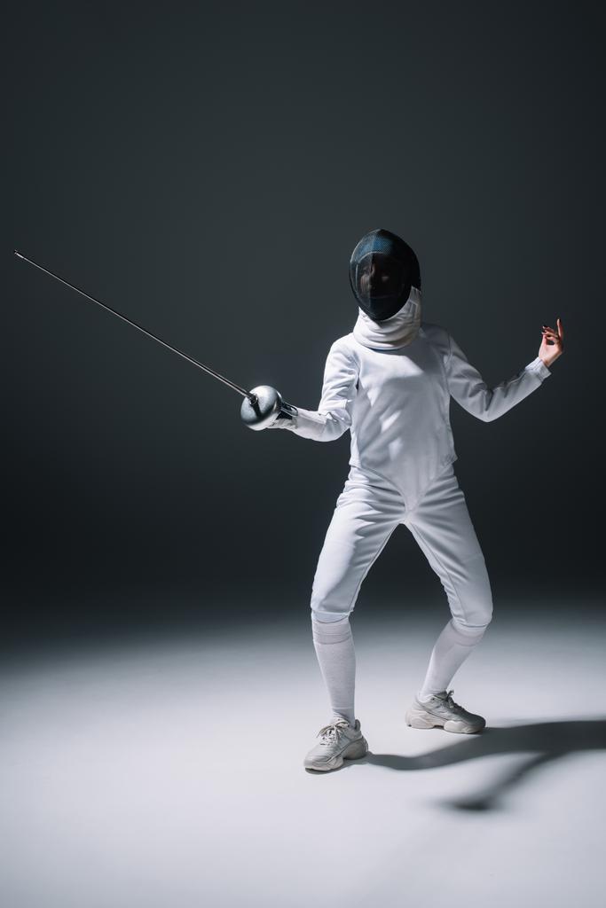 Fencer στην εκπαίδευση μάσκα ξιφασκίας με rapier σε λευκή επιφάνεια σε μαύρο φόντο - Φωτογραφία, εικόνα