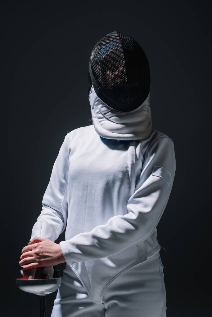 Esgrima em roupa de esgrima e máscara segurando rapier isolado em preto
  - Foto, Imagem