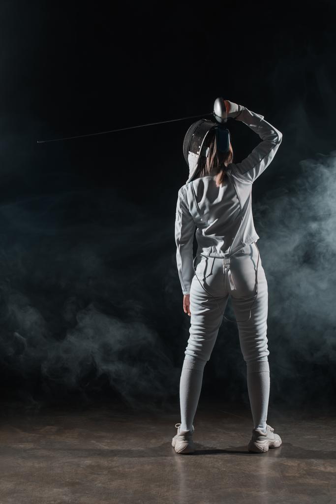 Back view of swordswoman fencing on black background with smoke  - Photo, Image