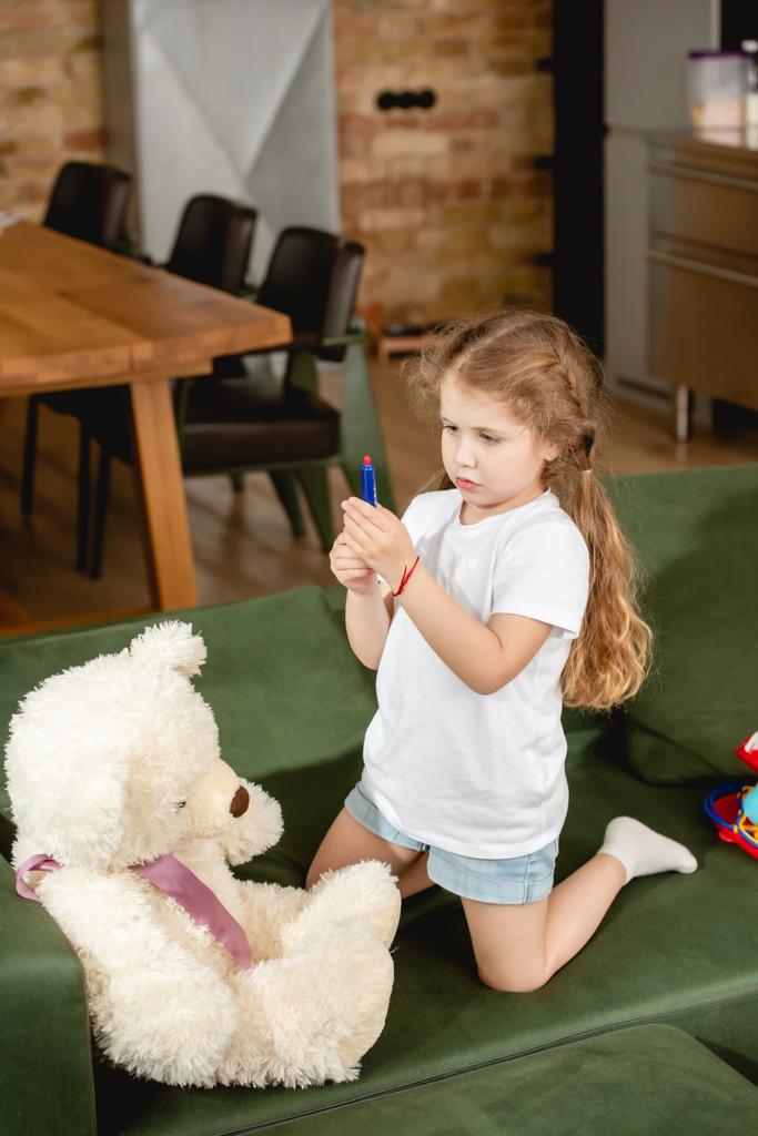 Niedliche Kind hält Spielzeug Spritze in der Nähe von Teddybär beim Spielen Arzt Spiel  - Foto, Bild