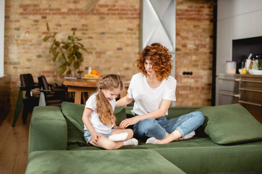 mãe encaracolado olhando para a filha sentada em pose de lótus no sofá
 - Foto, Imagem