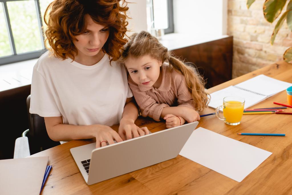 aranyos gyerek nézi laptop míg szabadúszó anya dolgozik otthonról  - Fotó, kép