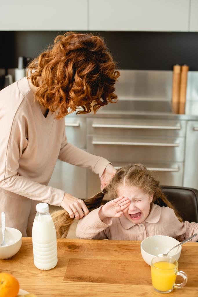 curly mother near upset daughter crying near breakfast  - Photo, Image