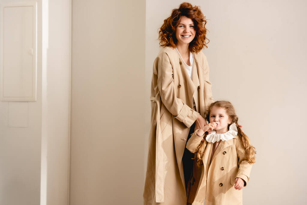 happy mother and cheerful kid standing in trench coats  - Photo, Image
