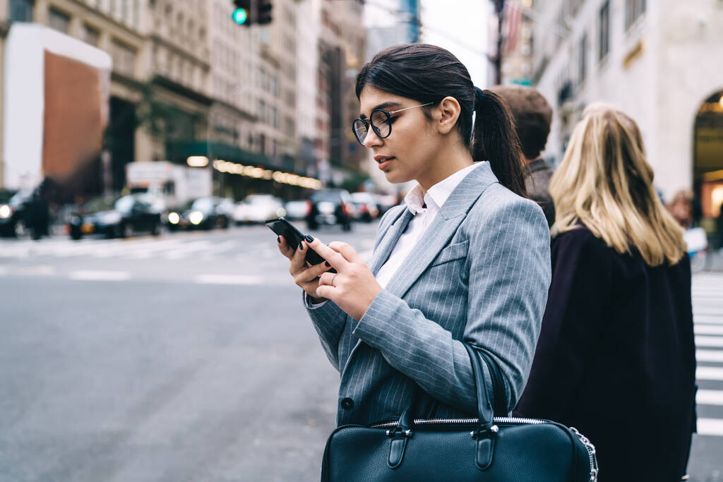 Junge Geschäftsfrau liest Finanznachrichten auf dem Weg zur Arbeit mit 4g-Verbindung auf modernem Mobiltelefon, hispanische Unternehmerin konzentriert sich auf das Schreiben von E-Mails mit Kontaktnummern - Foto, Bild