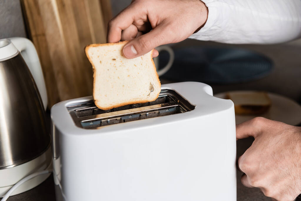 Вид человека, кладущего кусок хлеба в тостер
 - Фото, изображение