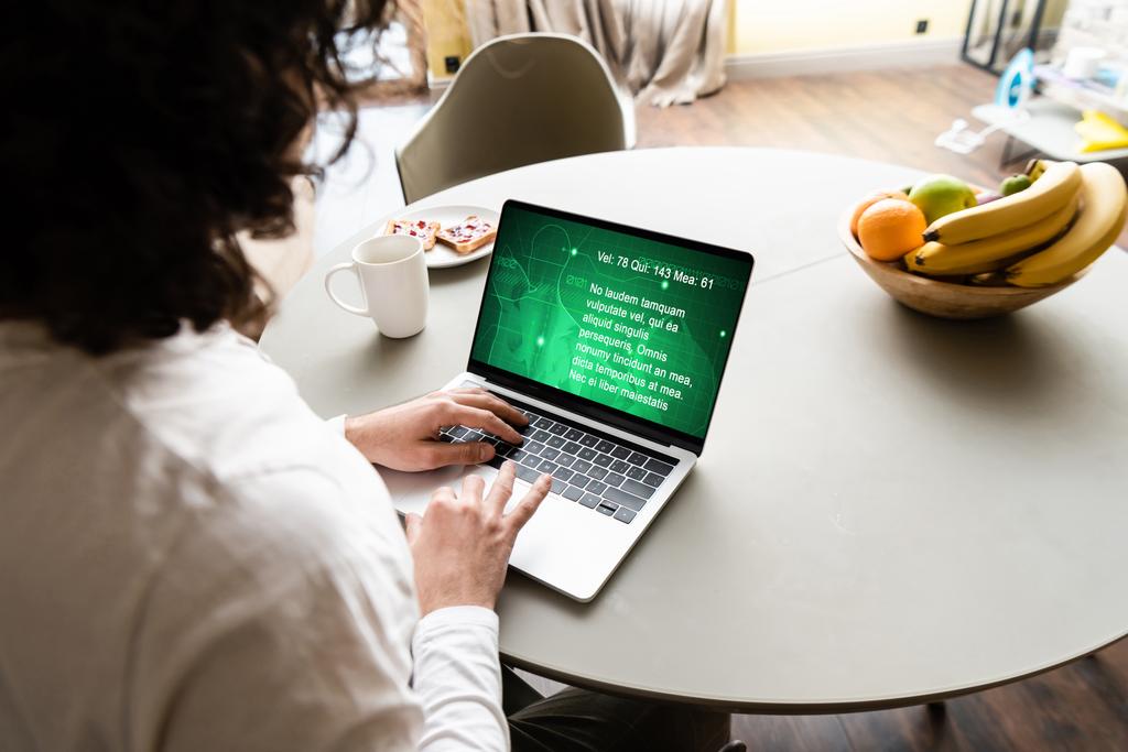 widok z tyłu freelancer za pomocą laptopa ze stroną medyczną w pobliżu owoców, filiżanka kawy i talerz z toastami - Zdjęcie, obraz