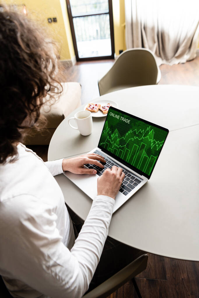 высокий угол зрения фрилансера с помощью ноутбука с онлайн-графики торговли возле чашки кофе и пластины с тостами
 - Фото, изображение