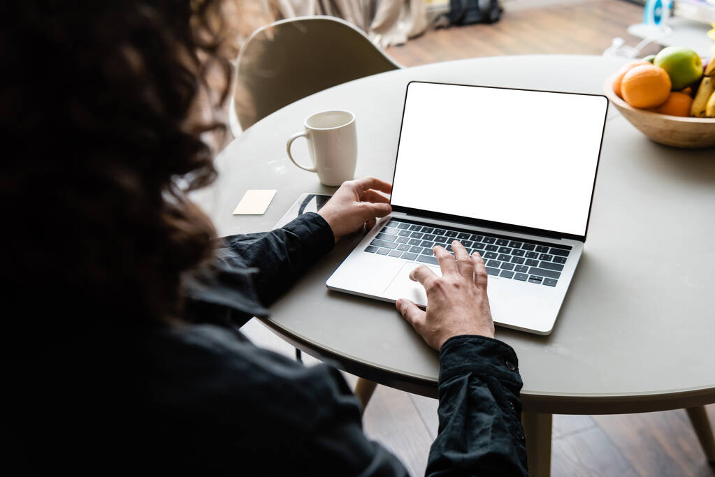 visão traseira do freelancer usando laptop com tela branca perto de xícara de café, notas pegajosas e frutas
 - Foto, Imagem