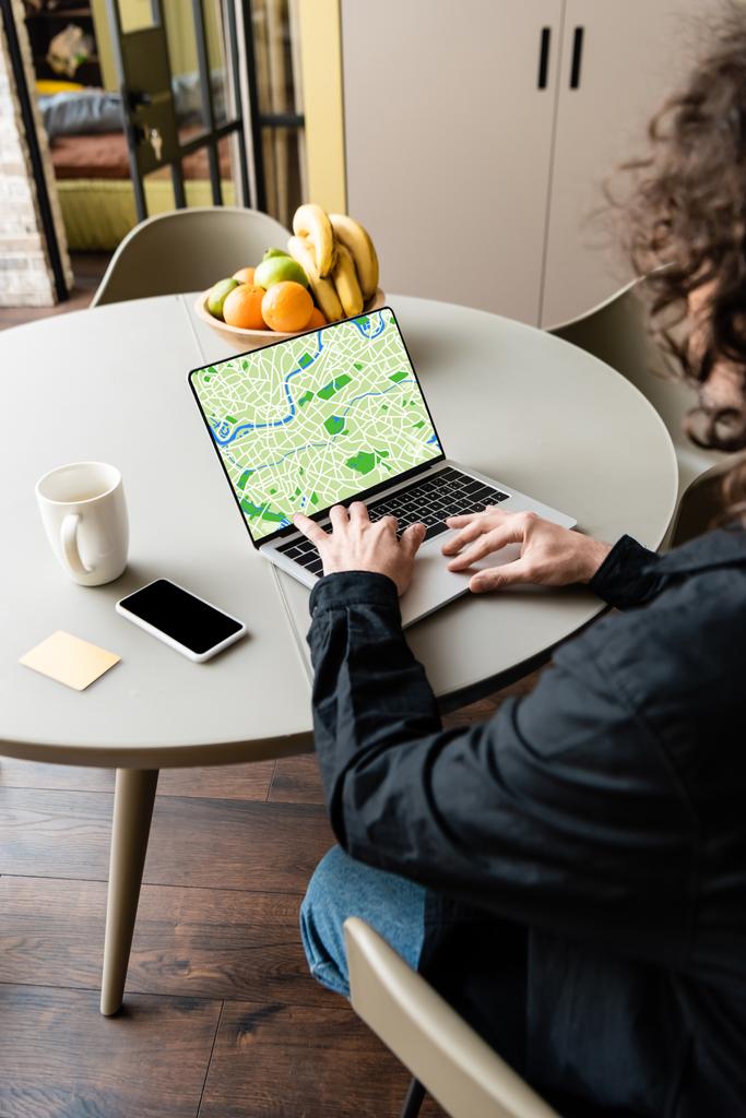 visszapillantás a szabadúszó használja laptop térképet a képernyőn közelében okostelefon, kávé csésze, ragadós megjegyzések és gyümölcsök - Fotó, kép