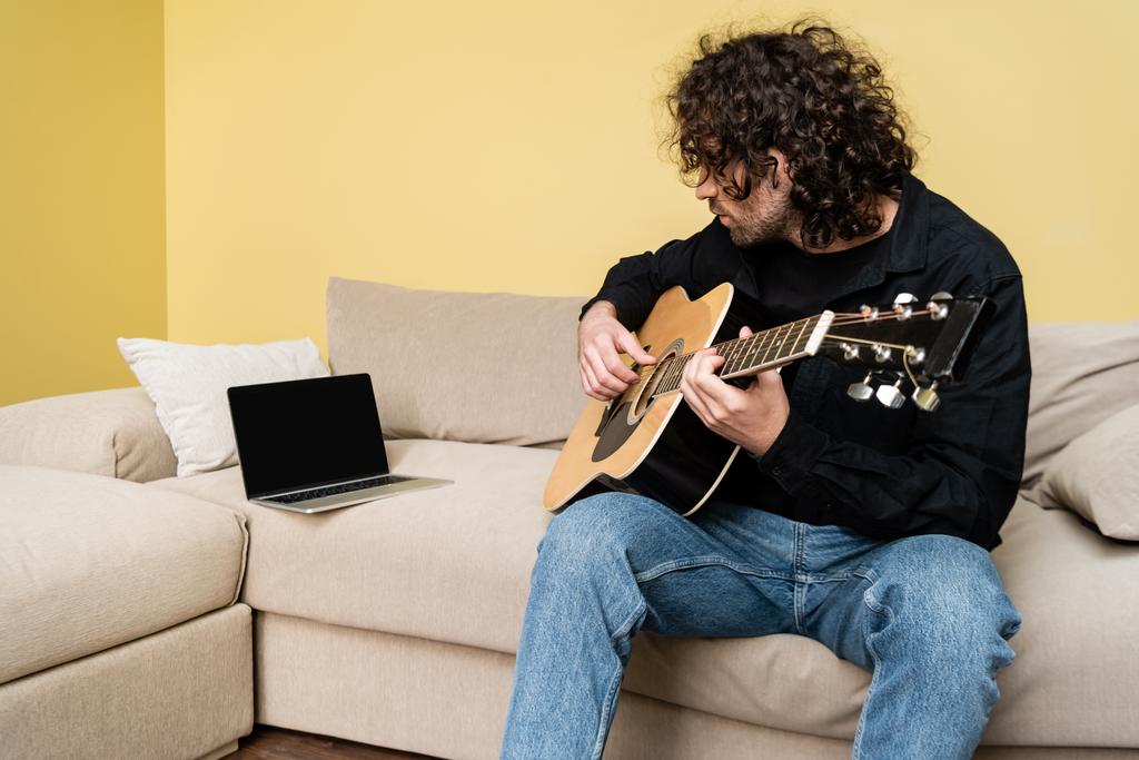 Человек, играющий на акустической гитаре во время вебинара на диване
  - Фото, изображение