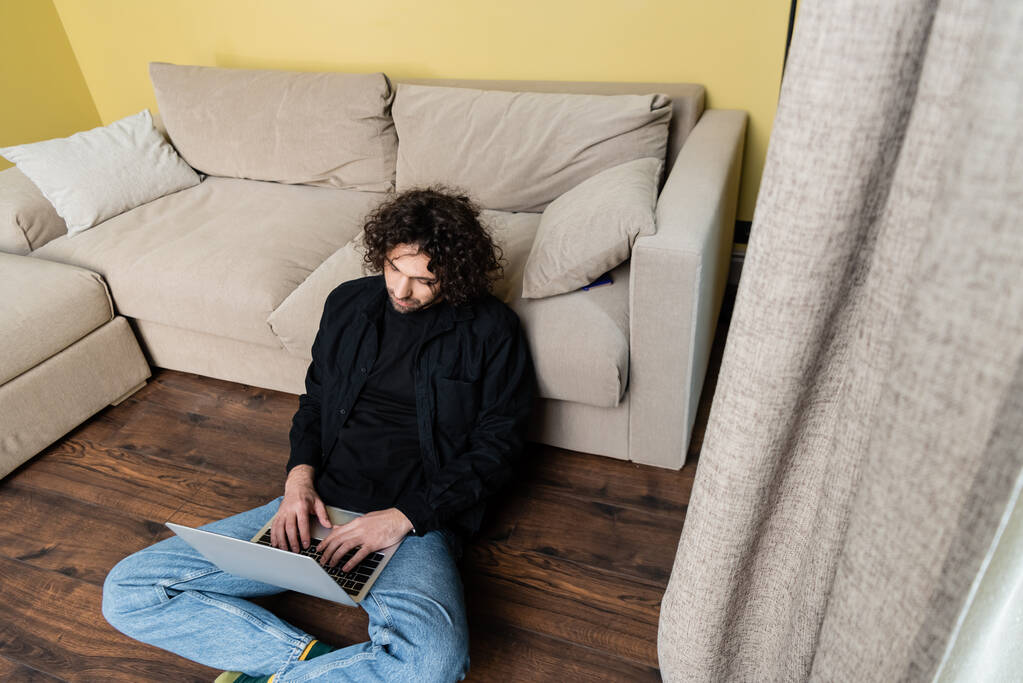Selektywne skupienie kręconego człowieka za pomocą laptopa na podłodze w domu  - Zdjęcie, obraz