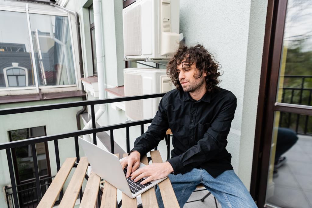 Guapo freelancer usando laptop en balcón en casa
  - Foto, imagen