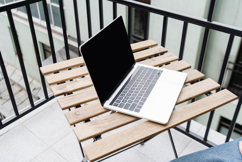 Widok człowieka siedzącego obok laptopa z pustym ekranem na stole na balkonie  - Zdjęcie, obraz