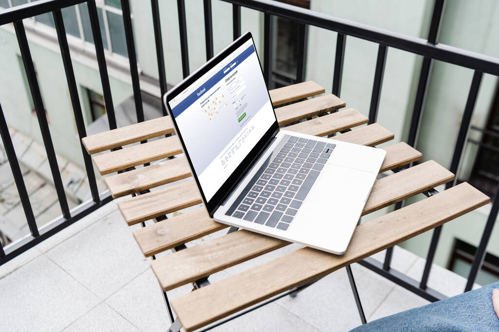 KYIV, UKRAINE - APRIL 25, 2020: Cropped view of man sitting near laptop with facebook website on balcony - Photo, Image