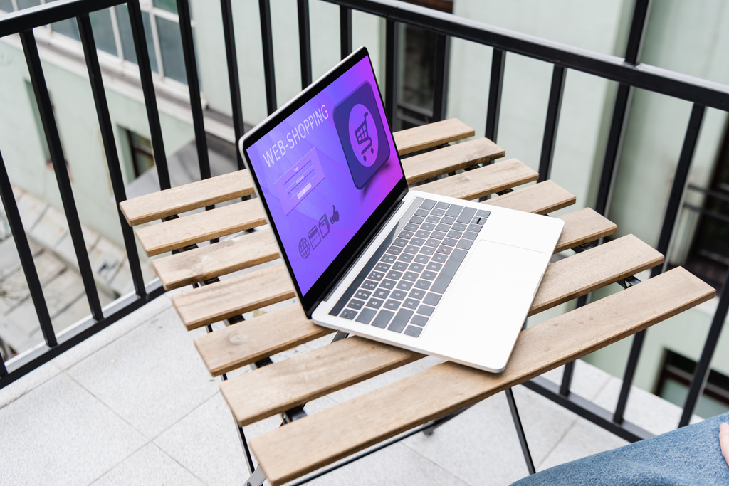 Widok człowieka siedzącego obok laptopa ze stroną internetową zakupy na balkonie  - Zdjęcie, obraz