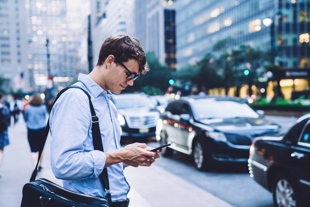 Сторона зору дорослого робітника в сорочці і окуляри серфінг смартфон під час подорожі по вулиці Нью-Йорка - Фото, зображення