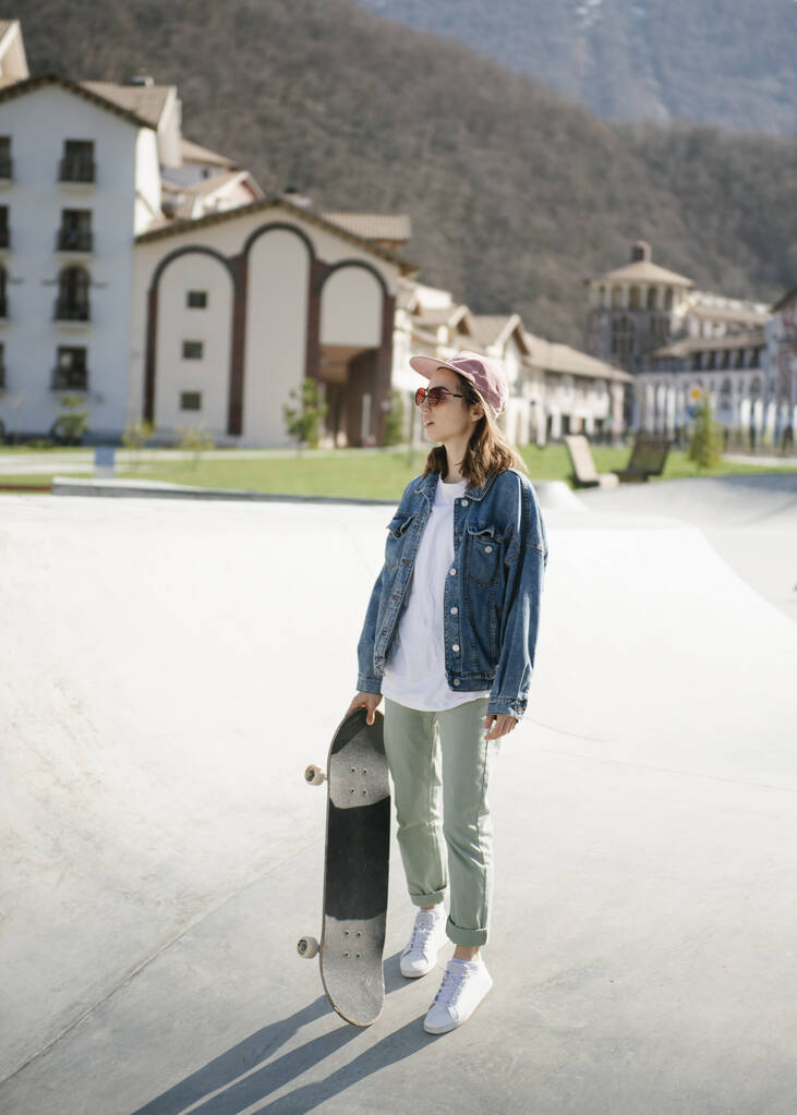 Молодая женщина со скейтбордом смотрит на улицу
 - Фото, изображение