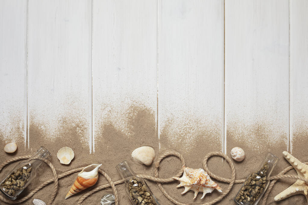Летний интерьер украшают морские звезды, ракушки, песок, веревки и бутылки с камнями на белом деревянном фоне. Принято. Натюрморт Плоский лежал
 - Фото, изображение