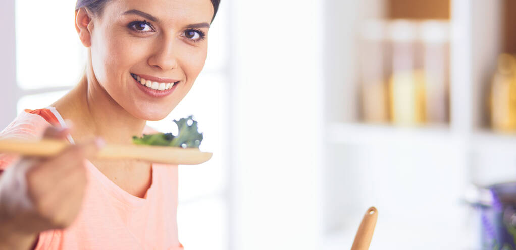 Sorrindo jovem mulher misturando salada fresca na cozinha. - Foto, Imagem